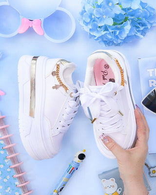 Tenis blancos suela gruesa con línea dorada y cadena al lado dorada con dijes